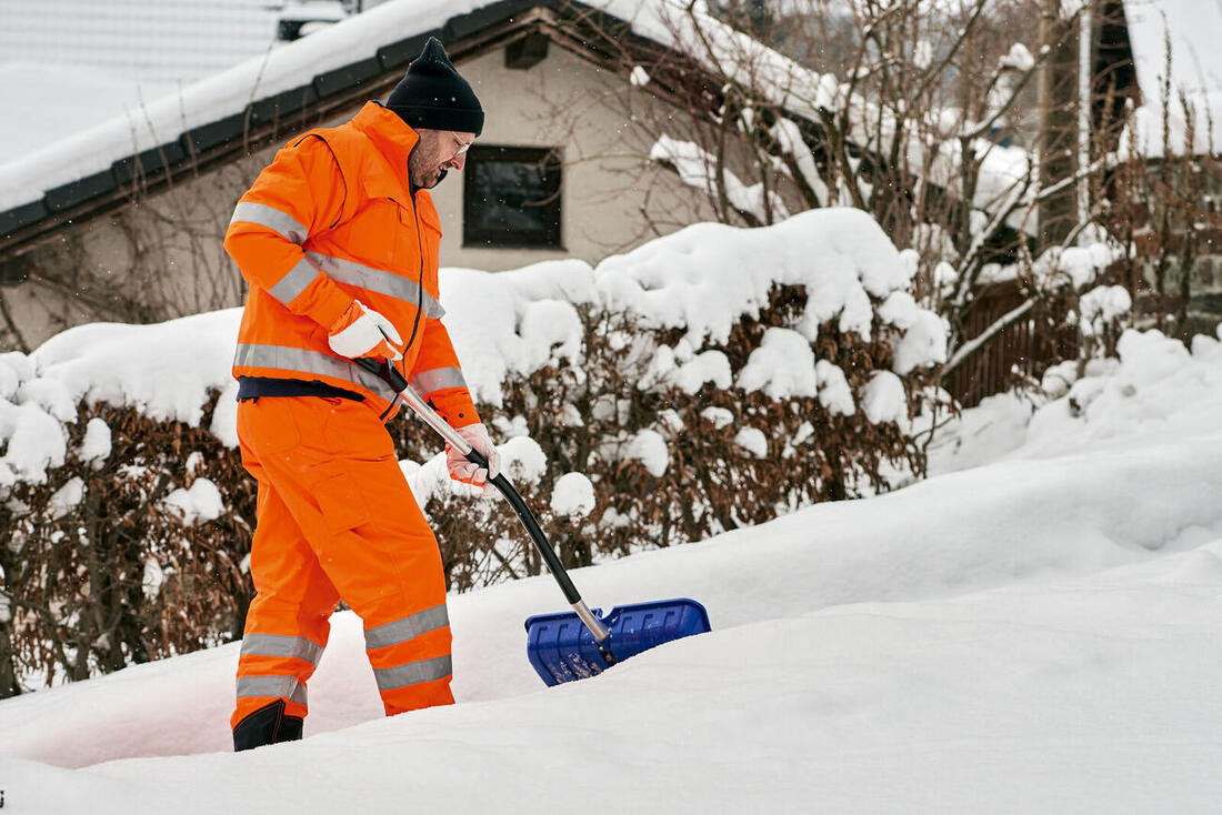 Mitarbeiter in Warnkleidung schiebt Schnee vor einem Hauseingang frei