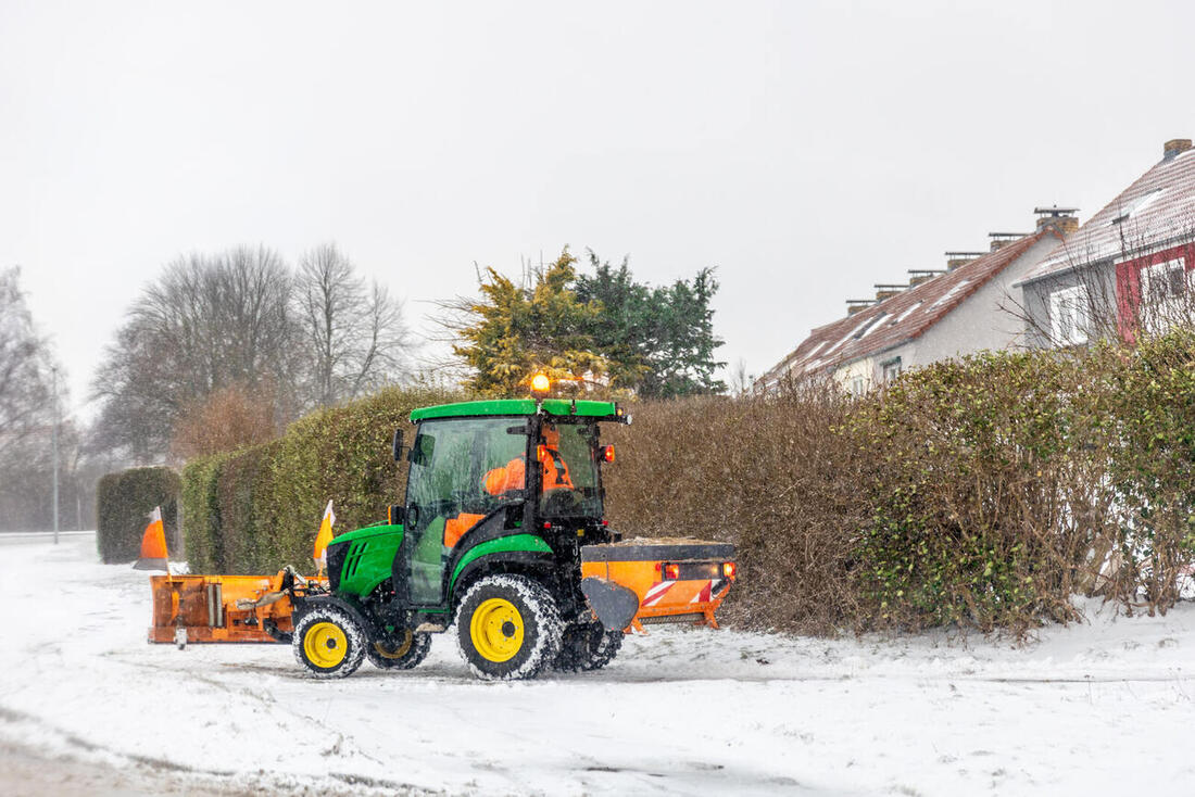 Kommunaltraktor mit Schneeschild und Streuer im Schneetreiben