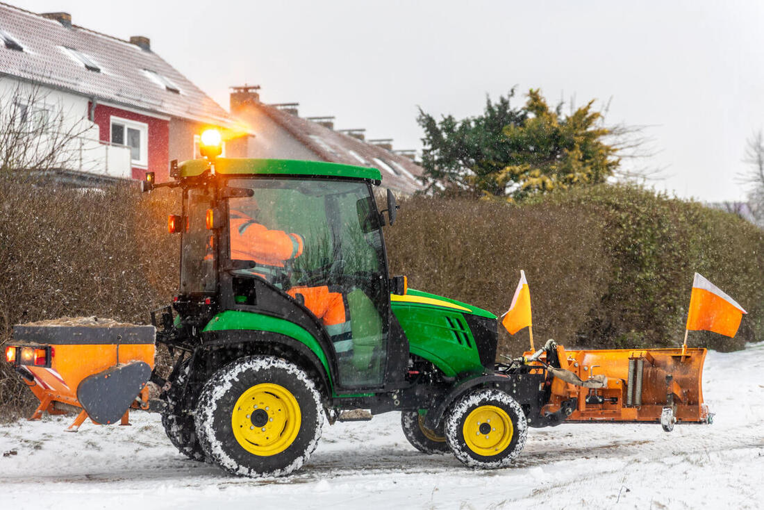 Traktor mit Schneepflug und Streuautomatik räumt eine Straße